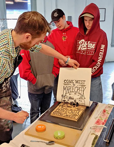 Artist Geoff Phillips demonstrates 'pulling a print' from a block as a hands-on illustration of the printing of posters at the turn of the last century. Geoff hand carved this print block to represent the style of settlement promotional posters that were common during the Settlement Boom era.