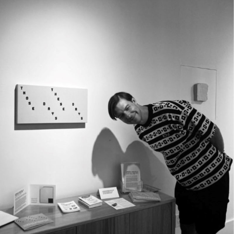 Jordan Danchilla - Man bending over from the waist smiling in from of art piece mounted on a wall in exhibition
