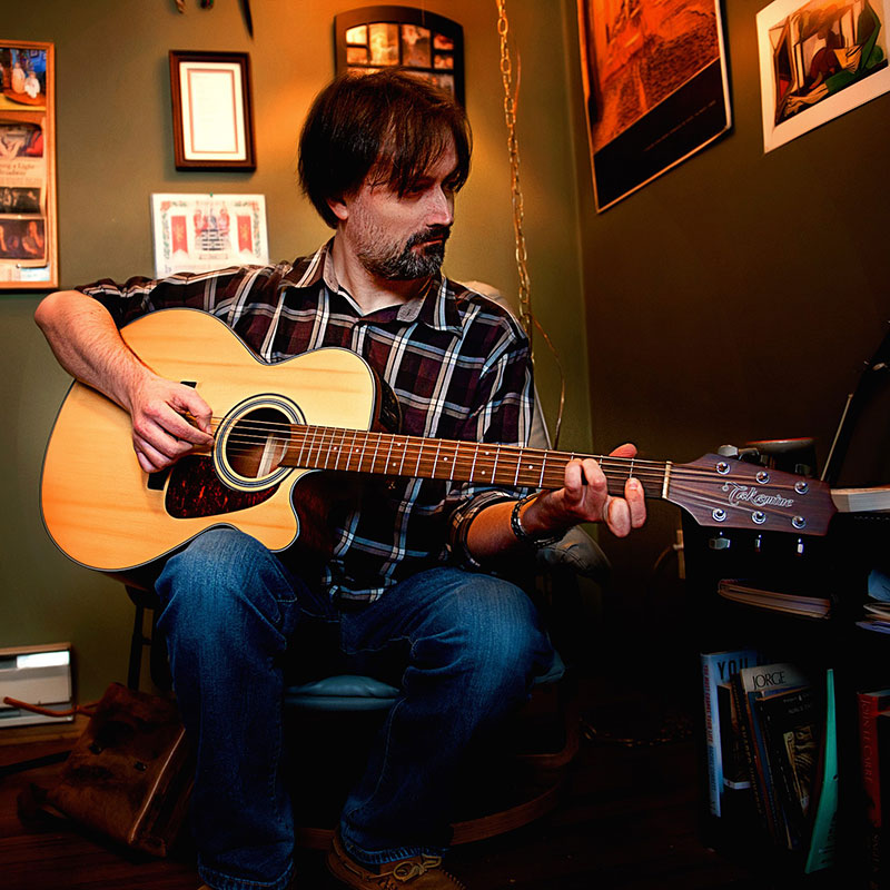 Kevin Imrie - Man with medium length brown hair and plaid shirt playing guitar