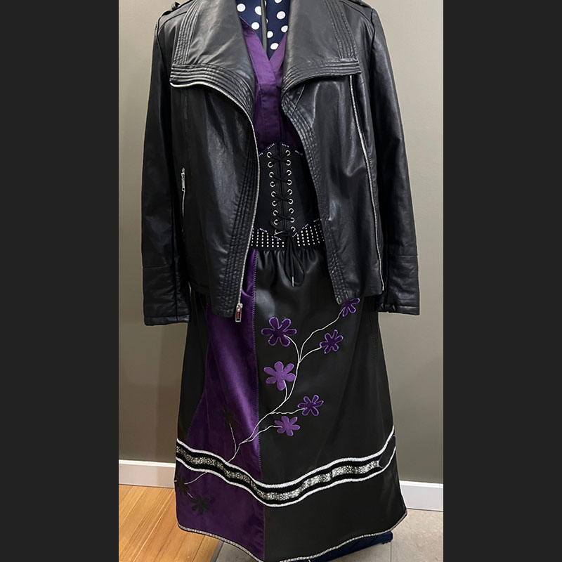  Black and purple story skirt, designed by Nancy Lafleur on a hanger with a leather jacket in front of a gray wall
