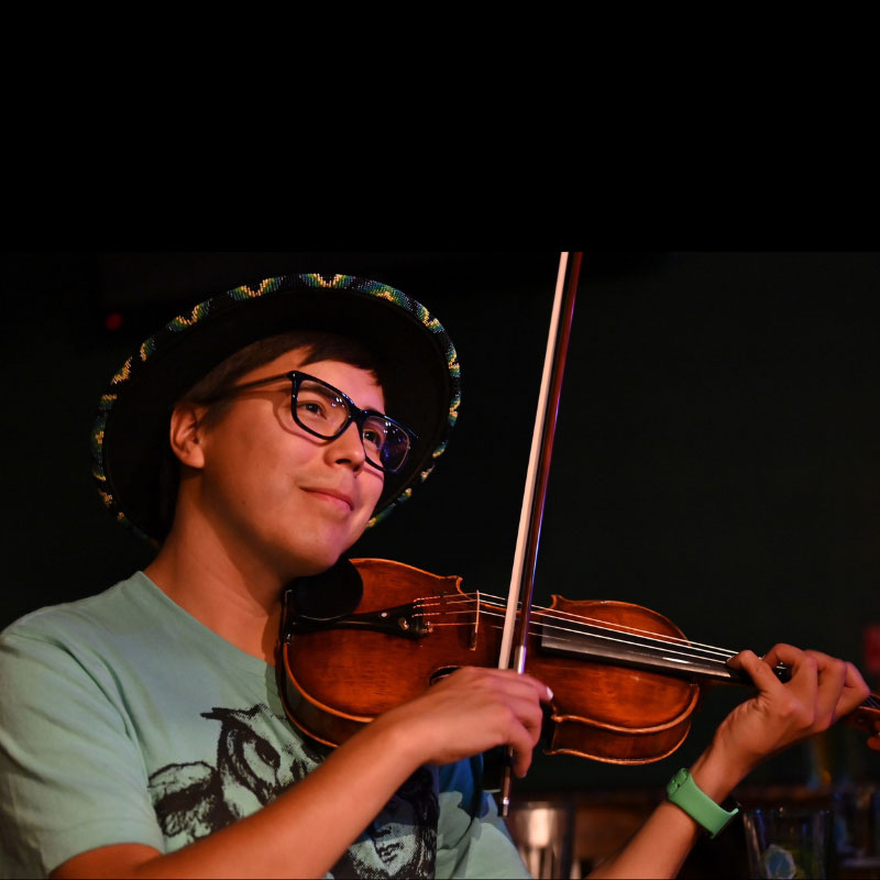 Tristen Durocher - Man wearing sombrero and playing the fiddle. He is wearing glasses and a green shirt.