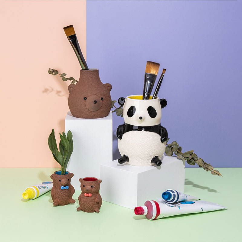 Ya-Li 'Bear' Won, - Picture of four ceramic bears staged as paintbrush holders and vases. There blue, red and yellow paint tubes and the base is pastel green with a pastel pink and lavender background.