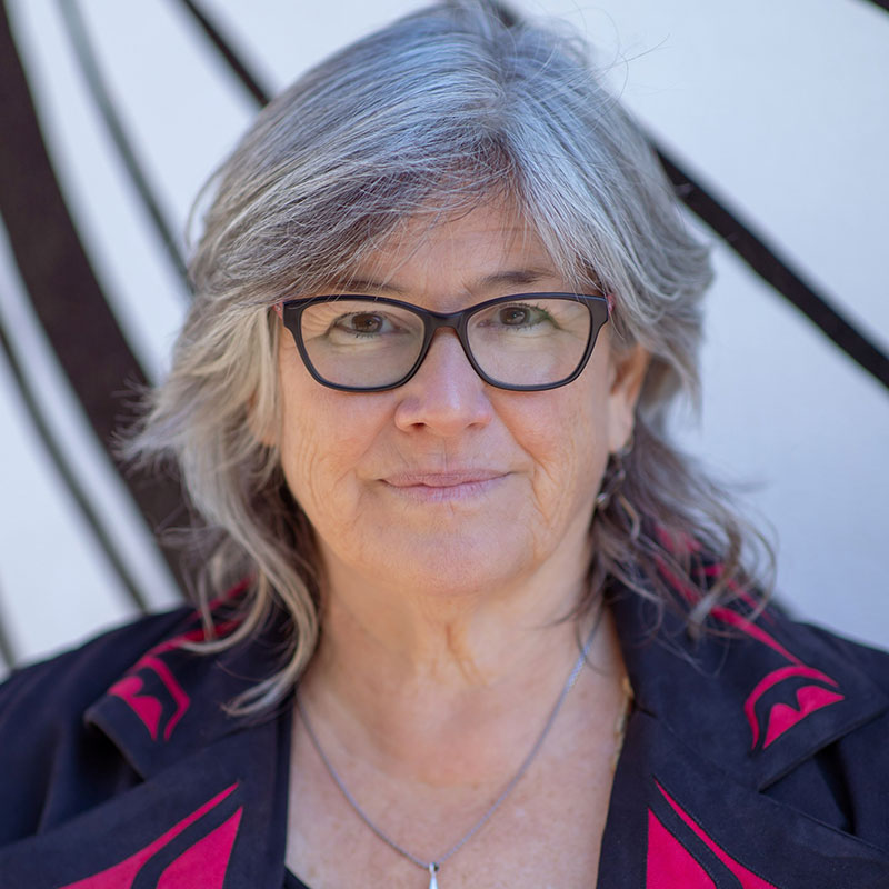 Yvette Nolan - Older white woman with gray hair wearing glasses and smiling