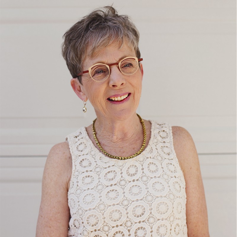 Ruth Smillie - Portrait photo of older woman with gray hair, wearing glasses, an ivory tank top