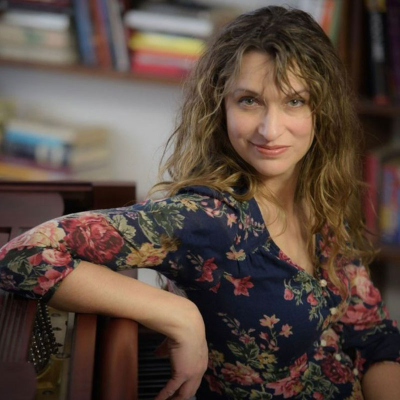 Dara Schindelka - Young woman with brown curly hair with a library behind her