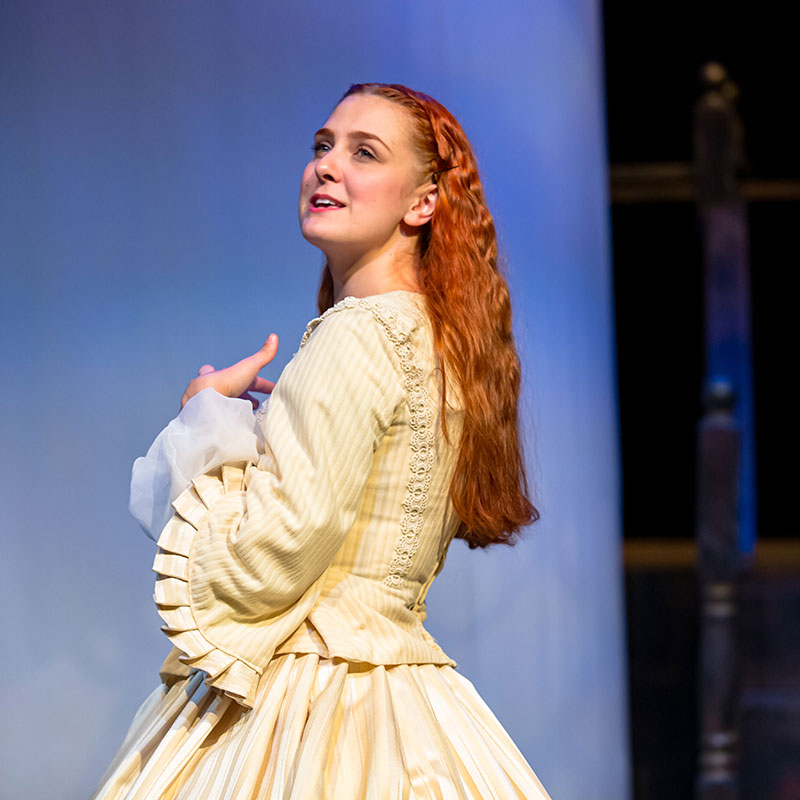 Elizabeth Chamberlain - Young woman with long red hair mid performance on a stage wearing a vintage yellow dress