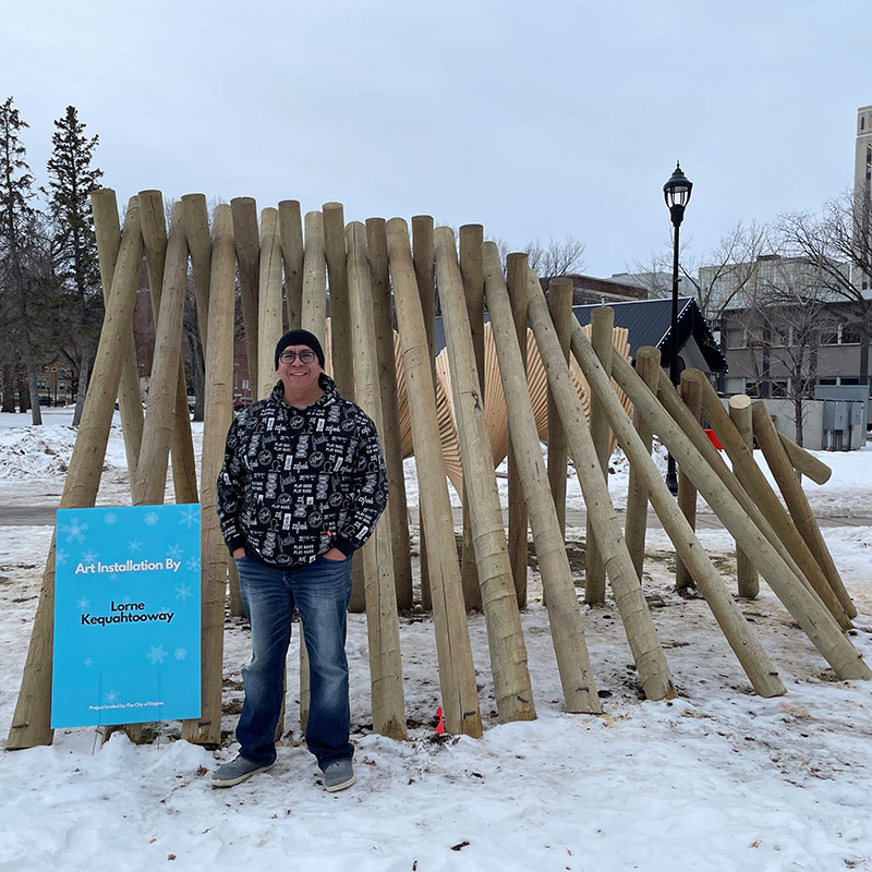 Lorne Kequahtooway - Man standing in front of a sculpture in winter