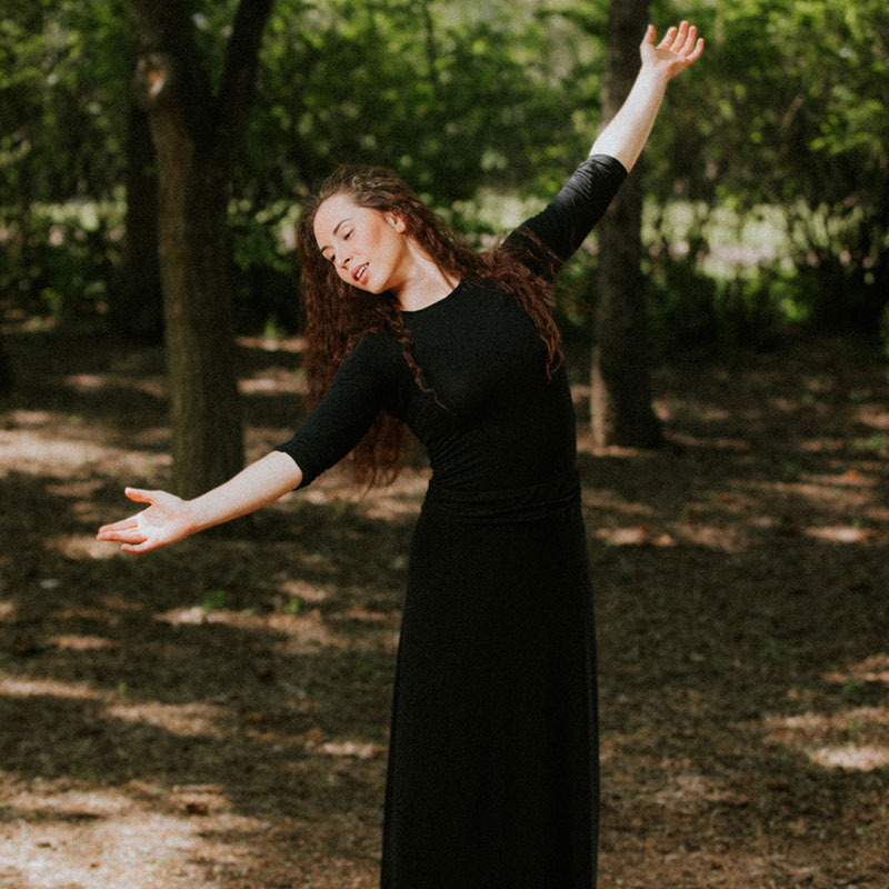 Tessa Rae Kuz - Young woman in long black dress in the woods mid-dance