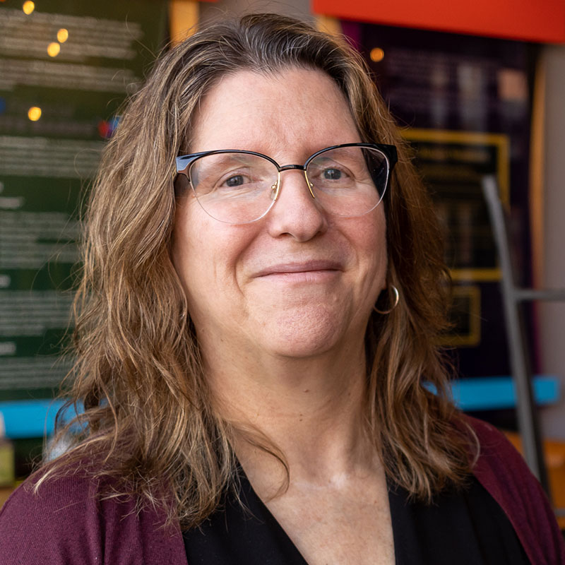 Joanne Weber - Woman with long brown curly hair wearing glasses and smiling