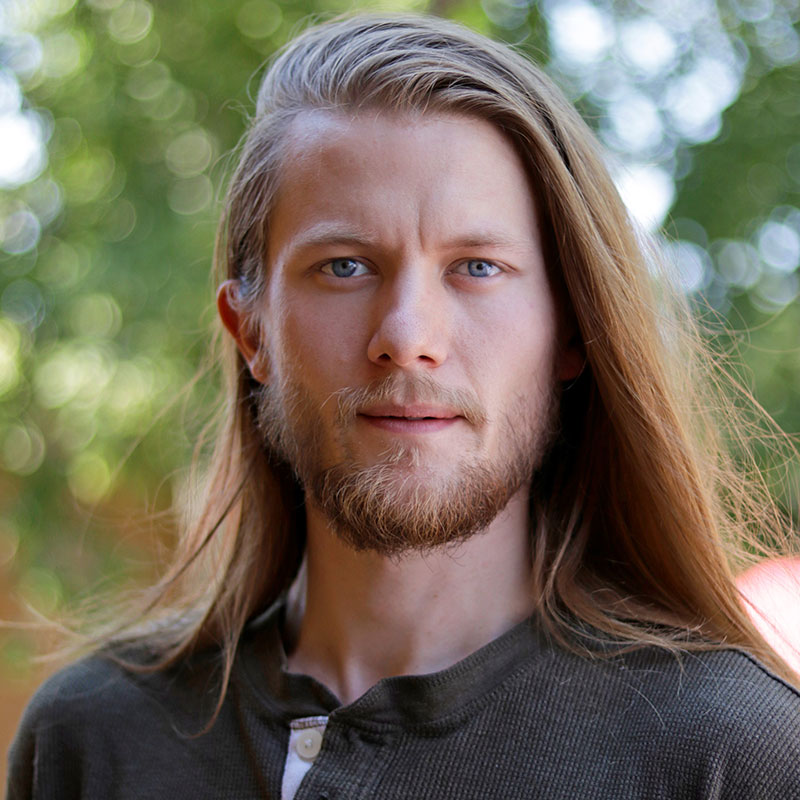 Zac Oliver - Portrait young man with long blonde hair and blue eyes wearing brown shirt