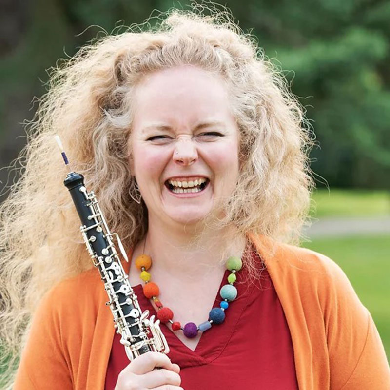 Erin Brophey - photo of blonde woman wearing an orange cardigan and red blouse and holding an oboe