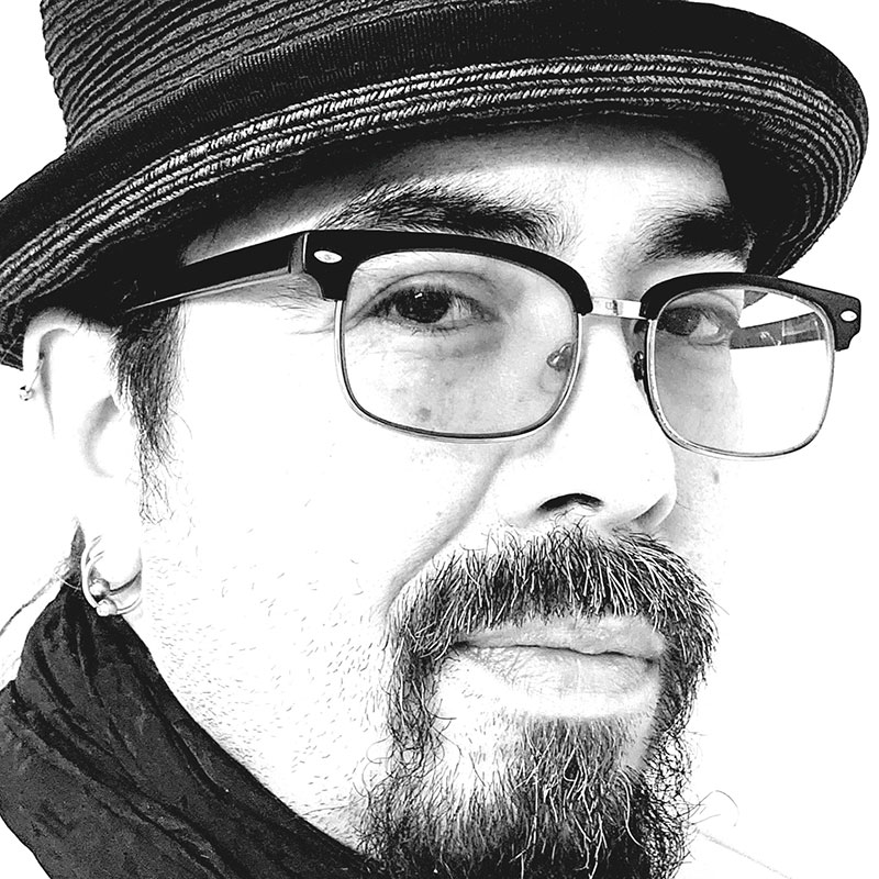 Michael Gamble - Black and white close up portrait of man wearing a hat, and glasses. He has a mustache and goatee
