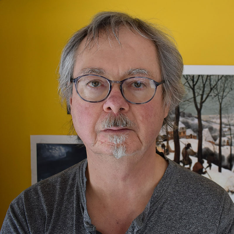 Michael Trussler - Older man with grey hair, eyebrows and mustache. He is wearing glasses and a grey t-shirt