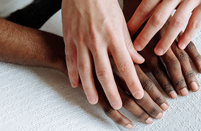 Picture of white person's hands lightly laying over black person's hands reading braille